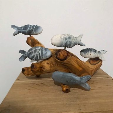 Holzskulptur mit mehreren dekorativen, grauen und weißen Fischen auf einem Baumstamm.