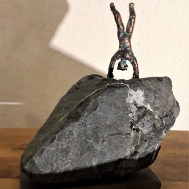 Eine Metallfigur, die auf einem großen Stein Handstand macht.