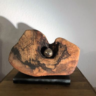 Holzskulptur mit einer runden Metallkugel in einer Vertiefung.