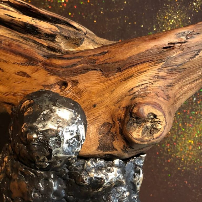 Holzskulptur mit metallischen Elementen, organische Formen und lebendige Farben im Hintergrund.