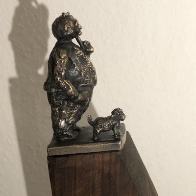 Eine bronzene Statue eines Mannes mit einem Hund auf einer Holzbasis.