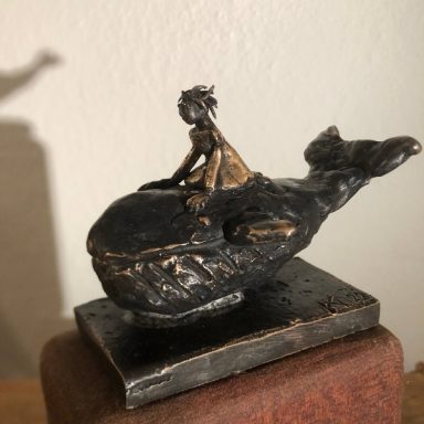 Bronzeskulptur eines Mädchens, das auf einem Walfisch sitzt, auf einem Holzsockel.